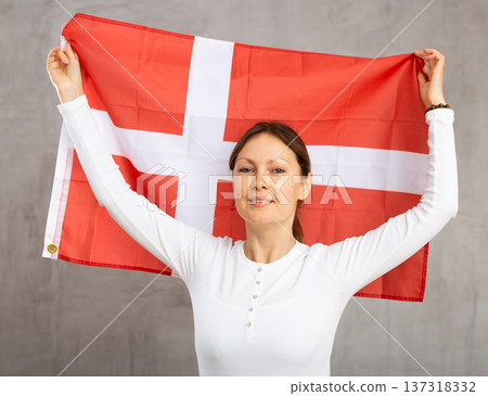 Happy young woman holding flag of Denmark against unicoloured background Happy young woman holding flag of Denmark against unicoloured background 137318332