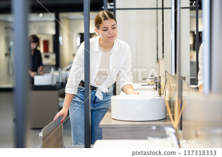 in plumbing department,thoughtful woman inspects round white ceramic sinks with faucets 137318333