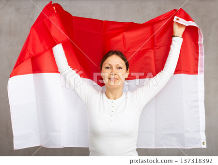 Happy young woman holding flag of Indonesia against unicoloured background 137318392