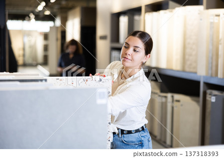 Satisfied young woman carefully chooses ceramic flooring for her apartment in hardware store Satisfied young woman carefully chooses ceramic flooring for her apartment in hardware store 137318393