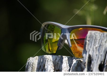 Reflective Sports Sunglasses With Orange Mirrored Lenses Resting On Weathered Wood In Sunlit Outdoor 137320401