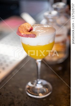 Alcoholic drink. Aperitif glass. Bright yellow tasty juice cocktail with white foam layer garnished with aromatic dried fruit slice. Alcoholic drink. Aperitif glass. Bright yellow tasty juice cocktail with white foam layer garnished with aromatic dried fruit slice. 137320737