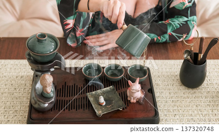 Chinese tea ceremony. Healthy lifestyle. Table with tea-board woman hand pouring water steam incense bowl for drinking figurine. Chinese tea ceremony. Healthy lifestyle. Table with tea-board woman hand pouring water steam incense bowl for drinking figurine. 137320748