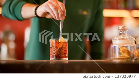Serving drink. Bartender work. Man adding orange carved peel in alcoholic refreshing beverage. Aromatic cold ice negroni cocktail. 137320977