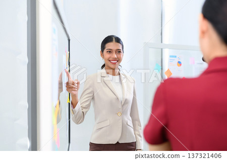 Businesswoman pointing towards graph and giving presentation explaining the idea to her business colleagues in the office. Group of Asian businesspeople brainstorm and work as team. 137321406
