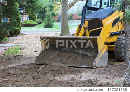 Yellow tractor is digging up dirt in yard surrounded by trees grass on sunny day Yellow tractor is digging up dirt in yard surrounded by trees grass on sunny day 137321566