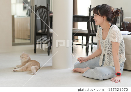 Happy asian woman sitting on indoor floor at home enjoying time with friendly pet cat promoting mental health wellness relaxing smiling expressing joyful positive emotion living room 137321970
