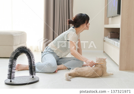 Happy asian woman using brush on friendly pet cat on floor at comfortable home improving mental health and everyday wellness during relaxing indoor activity for animal companion 137321971