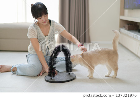 Young asian woman playing with pet cat at home supporting mental health wellness showing friendly emotion sitting on floor with toy arch groomer relaxing indoor environment feeling joyful 137321976