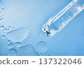 Dropper containing transparent skincare serum with bubbles on light blue liquid surface 137322046