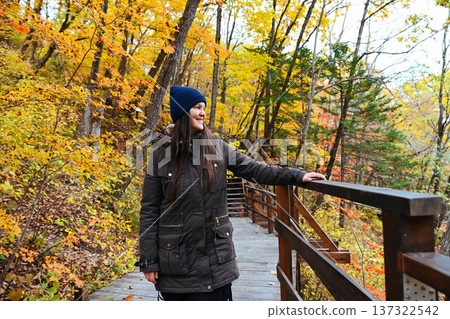 35-year-old woman standing on a wooden forest bridge in autumn, looking away. Horizontal outdoor travel photo with copy space and calm mood. 35-year-old woman standing on a wooden forest bridge in autumn, looking away. Horizontal outdoor travel photo with copy space and calm mood. 137322542