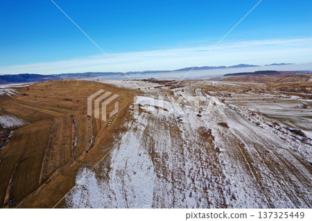 Aerial view of melting snow on hills on a misty sunny day Aerial view of melting snow on hills on a misty sunny day 137325449