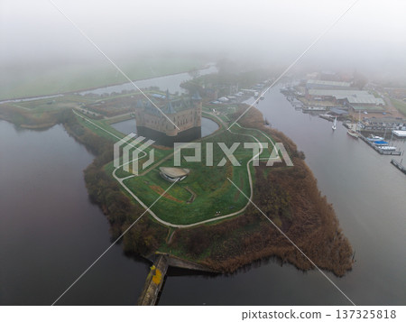 Aerial view of Muiderslot Castle in the fog. Historic medieval Dutch fortress surrounded by a moat and morning mist. Atmospheric drone shot of a winter landscape in Muiden, Netherlands. Aerial view of Muiderslot Castle in the fog. Historic medieval Dutch fortress surrounded by a moat and morning mist. Atmospheric drone shot of a winter landscape in Muiden, Netherlands. 137325818