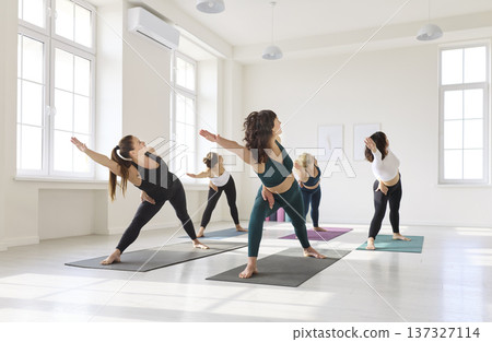 Women stretching in group yoga class, triangle pose alignment in airy studio Women stretching in group yoga class, triangle pose alignment in airy studio 137327114