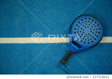 Padel racket sits on blue court with white line in warm light 137328022