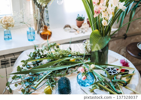 Floral arrangements with gladiolus stand on table surrounded by tools and greenery. Slow flower movement, seasonal blooms, local flower farming, eco-conscious floristry. Floral arrangements with gladiolus stand on table surrounded by tools and greenery. Slow flower movement, seasonal blooms, local flower farming, eco-conscious floristry. 137328037