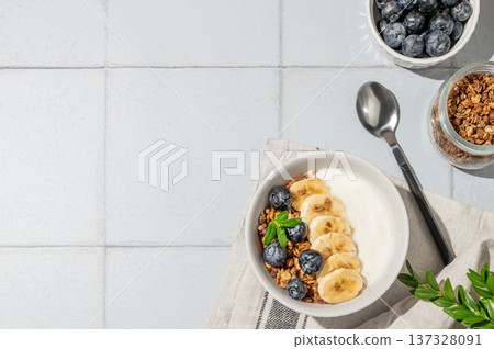 Greek yogurt with granola, blueberry and banana in a bowl on a blue tile background with berry 137328091