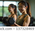 Young woman learning dumbbell exercises from gym trainer 137328469