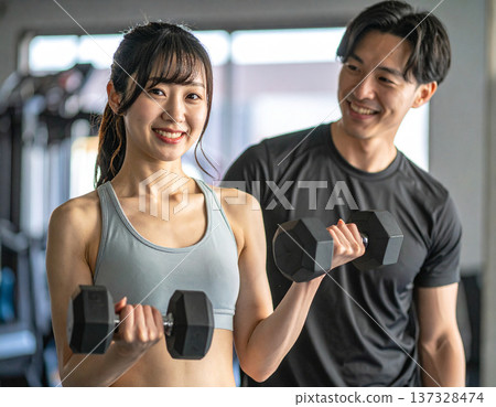 Young woman learning dumbbell exercises from gym trainer 137328474