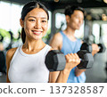 Young woman learning dumbbell exercises from gym trainer 137328587