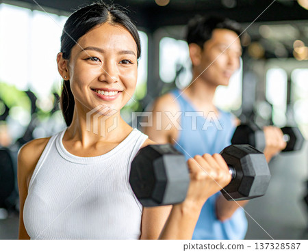 Young woman learning dumbbell exercises from gym trainer 137328587