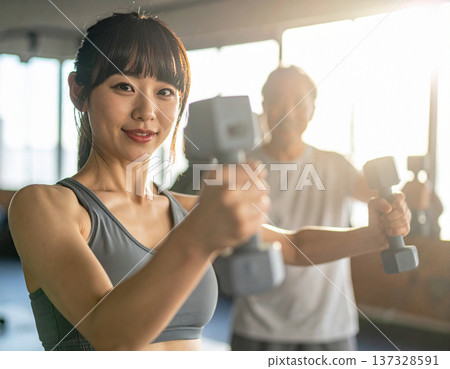Young woman learning dumbbell exercises from gym trainer 137328591