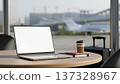 White screen laptop with coffee and books on wooden table and luggage at glass wall in airport cafe. 137328967