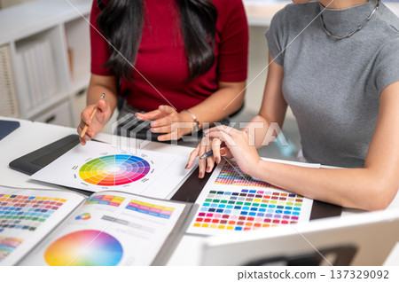 Close up of woman holding pencil talking to coworker over color chart as sitting at table in office. Close up of woman holding pencil talking to coworker over color chart as sitting at table in office. 137329092
