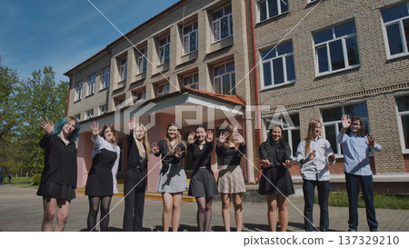 Energetic teens joyfully waving and celebrating the conclusion of the school year outside their high school 137329210