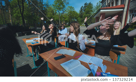 Happy students at outdoor desks raising their hands to celebrate the end of the school day Happy students at outdoor desks raising their hands to celebrate the end of the school day 137329214