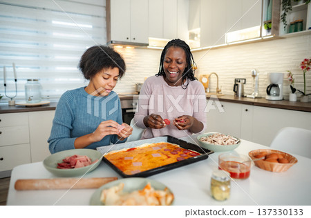 African American mother daughter making homemade pizza in kitchen 137330133