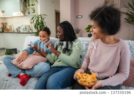 Friends enjoy a cozy afternoon together, laughing and sharing stories in a warm living room full of plants and comfort Friends enjoy a cozy afternoon together, laughing and sharing stories in a warm living room full of plants and comfort 137330196