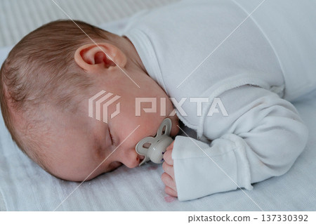 Close-up of newborn baby sleeping quietly with pacifier. Soft natural light and gentle shadows. Concept of night rest, calm atmosphere and healthy infant sleep routine. 137330392
