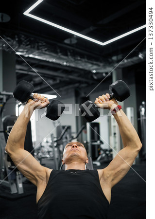 Strong man doing dumbbell bench press in gym 137330494