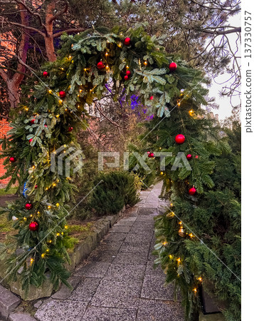 Festive archway made of greenery with lights and ornaments on a winter evening Festive archway made of greenery with lights and ornaments on a winter evening 137330757
