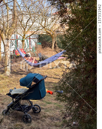 Person relaxing in hammock in backyard with stroller Person relaxing in hammock in backyard with stroller 137331942