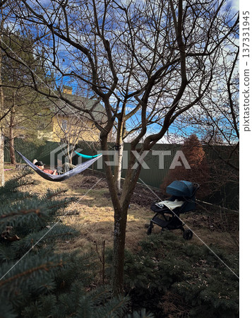 Person relaxing in hammock in backyard with stroller Person relaxing in hammock in backyard with stroller 137331945