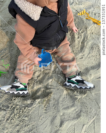 Toddler playing in sandbox holding blue sand mold Toddler playing in sandbox holding blue sand mold 137331951