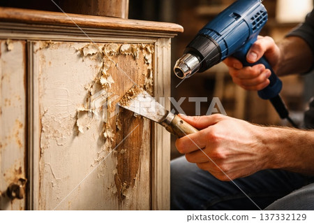 Worker stripping old paint from wooden cabinet with heat gun and scraper tool Worker stripping old paint from wooden cabinet with heat gun and scraper tool 137332129