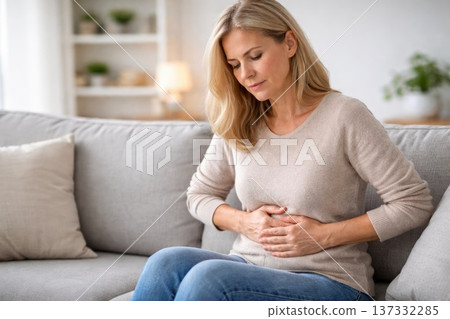 Middle aged woman holding stomach feeling abdominal pain while sitting at home Middle aged woman holding stomach feeling abdominal pain while sitting at home 137332285