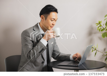 A businessman looking at a computer while drinking coffee 137333473