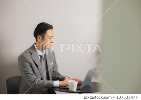A businessman looking at a computer while drinking coffee A businessman looking at a computer while drinking coffee 137333477