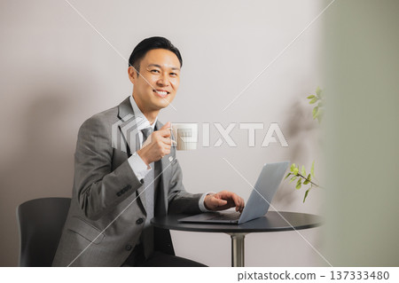 A businessman looking at a computer while drinking coffee A businessman looking at a computer while drinking coffee 137333480