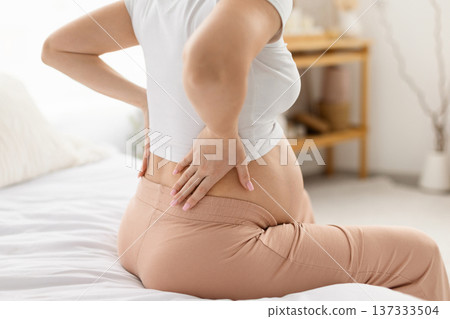 Close up of pregnant woman touching lower back while sitting on bed Close up of pregnant woman touching lower back while sitting on bed 137333504
