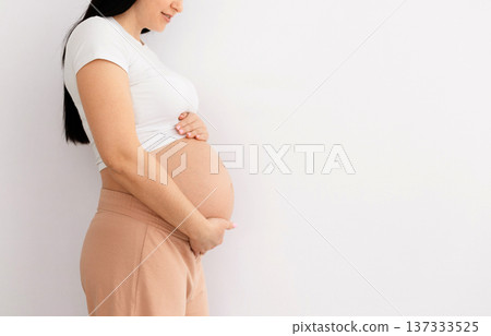 Young pregnant woman standing sideways at home gently holding belly Young pregnant woman standing sideways at home gently holding belly 137333525