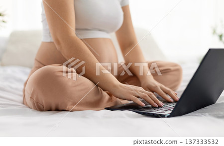 Pregnant woman sitting cross legged on bed using laptop at home 137333532