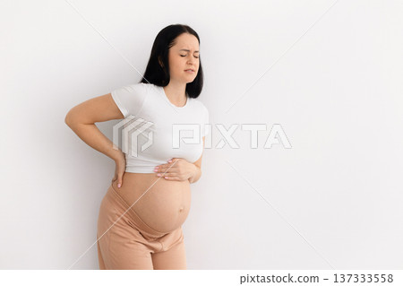 Pregnant woman standing at home holding belly and lower back with discomfort 137333558