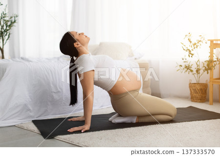 Pregnant woman practicing prenatal yoga back stretch on yoga mat at home 137333570