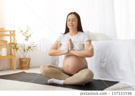 Young pregnant woman sitting on yoga mat with hands in prayer pose Young pregnant woman sitting on yoga mat with hands in prayer pose 137333596