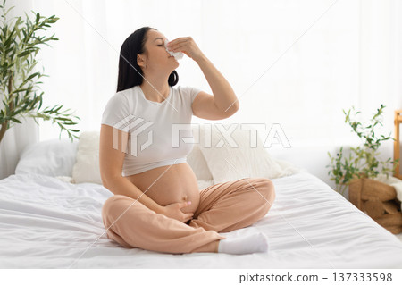 Pregnant woman blowing nose with tissue while feeling sick at home 137333598